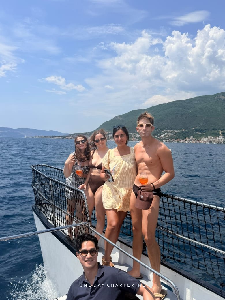 Guests on the bow of the catamaran with the Montenegrin coast behind them