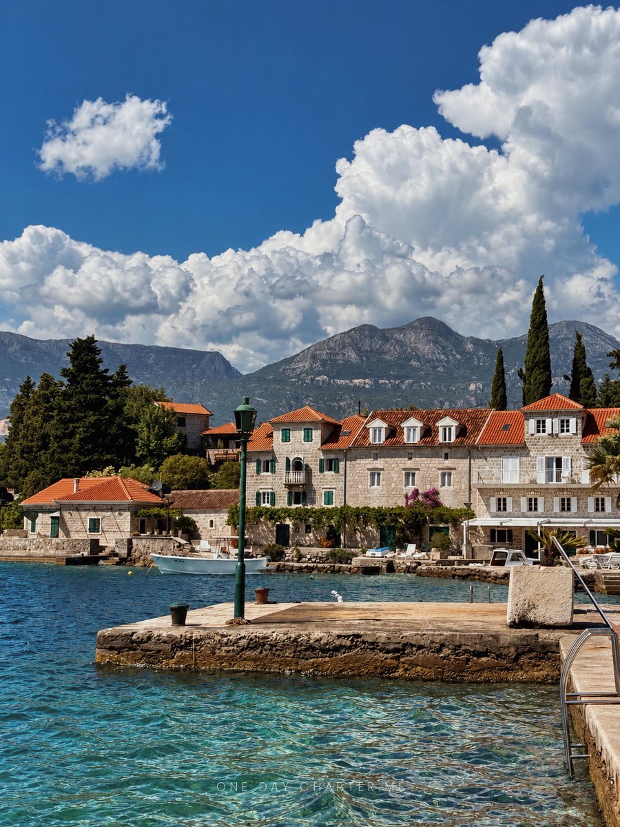 The stone waterfront of Rose on the Luštica peninsula, with old houses and the mountains of the Bay of Kotor behind